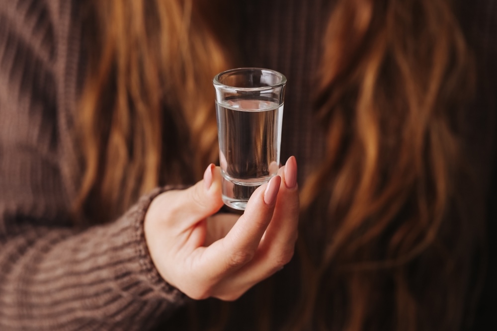 Female holding a shot of alcohol wondering how many shots to get drunk