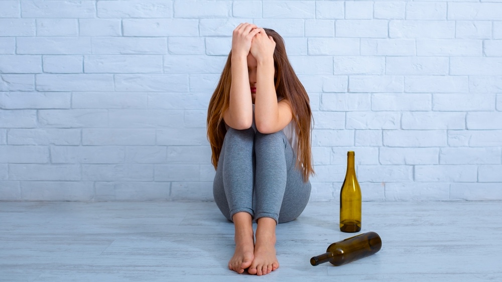 Female who relapsed sitting on the floor with empty wine bottles